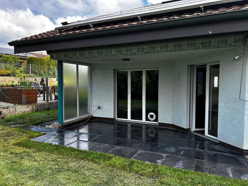 Modern house exterior with large glass sliding doors, tiled patio, and well-maintained lawn.