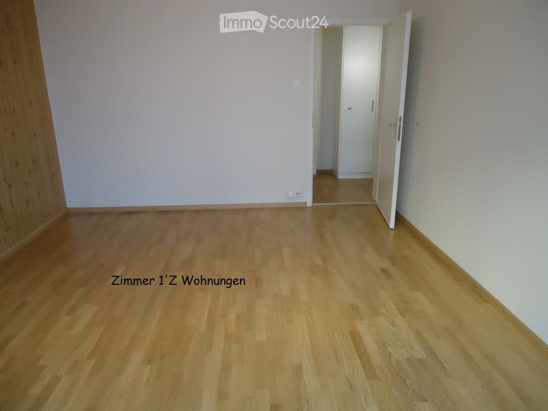 Empty room with light wooden flooring and white walls, featuring an open doorway leading to another space.