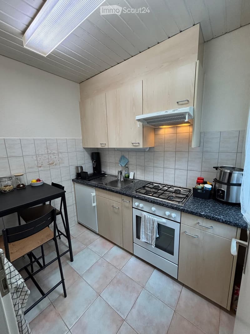Modern kitchen with light wood cabinets, granite countertops, gas stove, oven, sink, and a small dining area with a table and chairs.