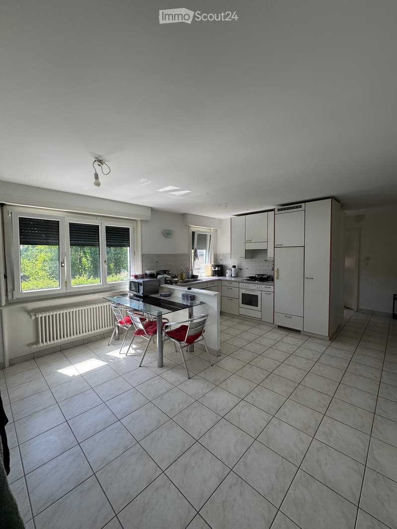 Modern kitchen with white cabinets, tiled floor, and large windows. Includes a dining area with a glass table and red chairs.