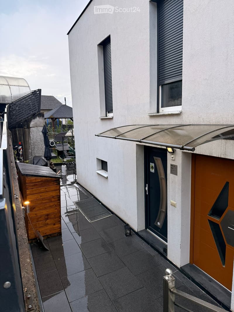 Balcony area with tiled flooring, modern awning, wooden shed, and outdoor furniture in the background.