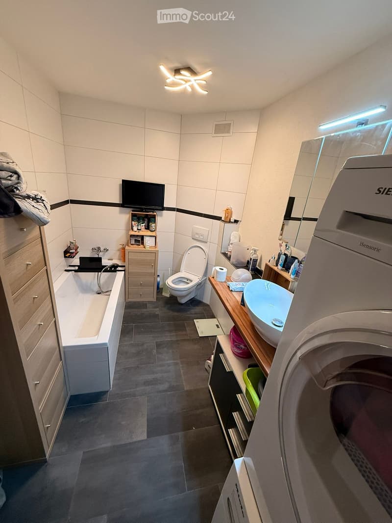 Modern bathroom with a bathtub, toilet, sink, and a large mirror. Features include a wooden cabinet, a screen, and a light fixture on the ceiling.