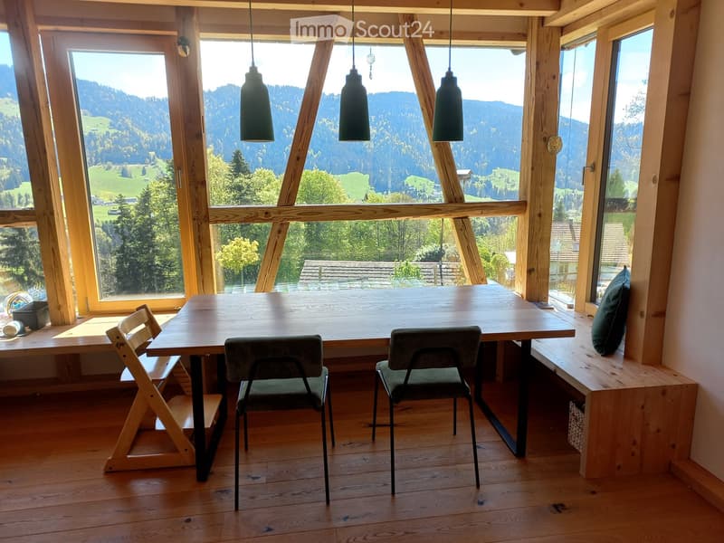 Bright dining area with large windows offering a scenic mountain view, featuring a wooden table, chairs, and a built-in bench.