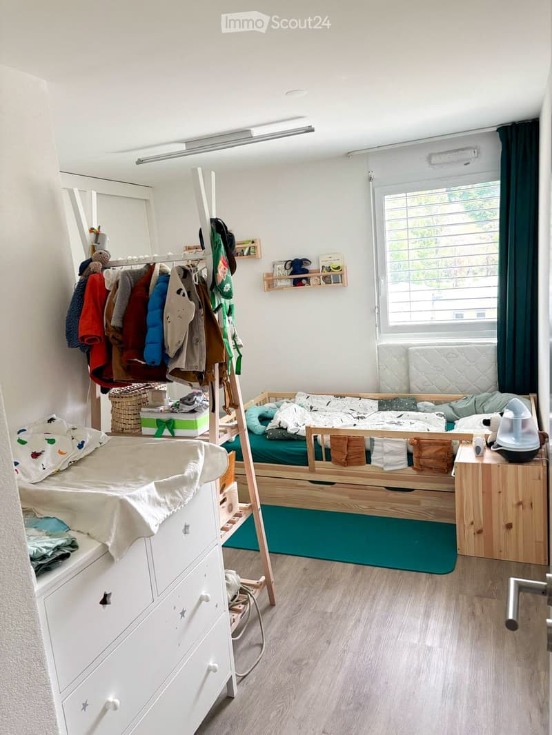 Cozy children's bedroom with two single beds, a wardrobe, shelves, and toys.