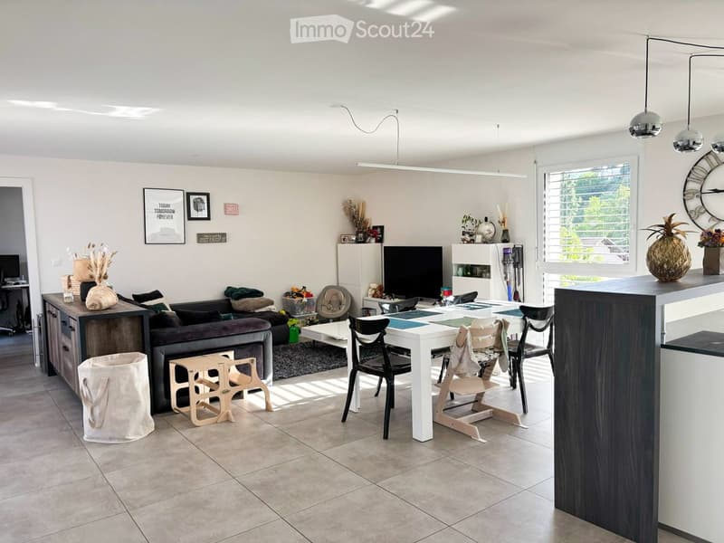 Modern living room with a sofa, coffee table, dining table, chairs, and decorative items. Features large windows and a sleek design.