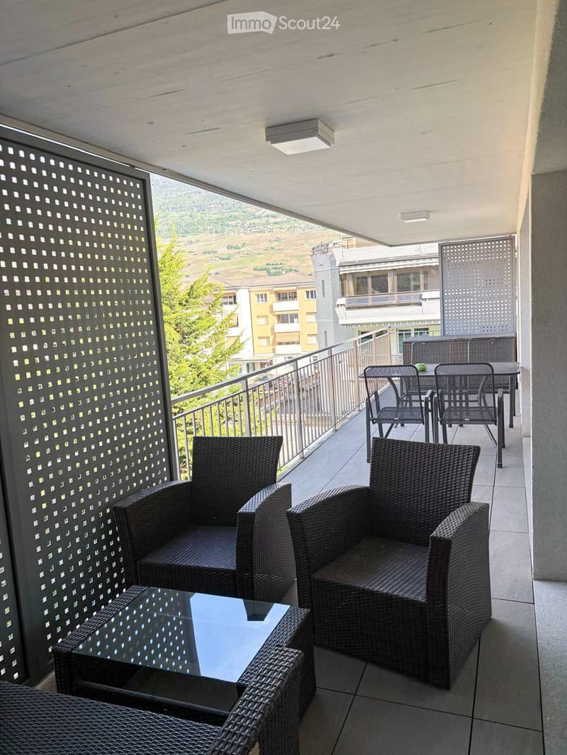 Balcony with wicker chairs, a glass coffee table, and a small dining set, overlooking a scenic landscape.