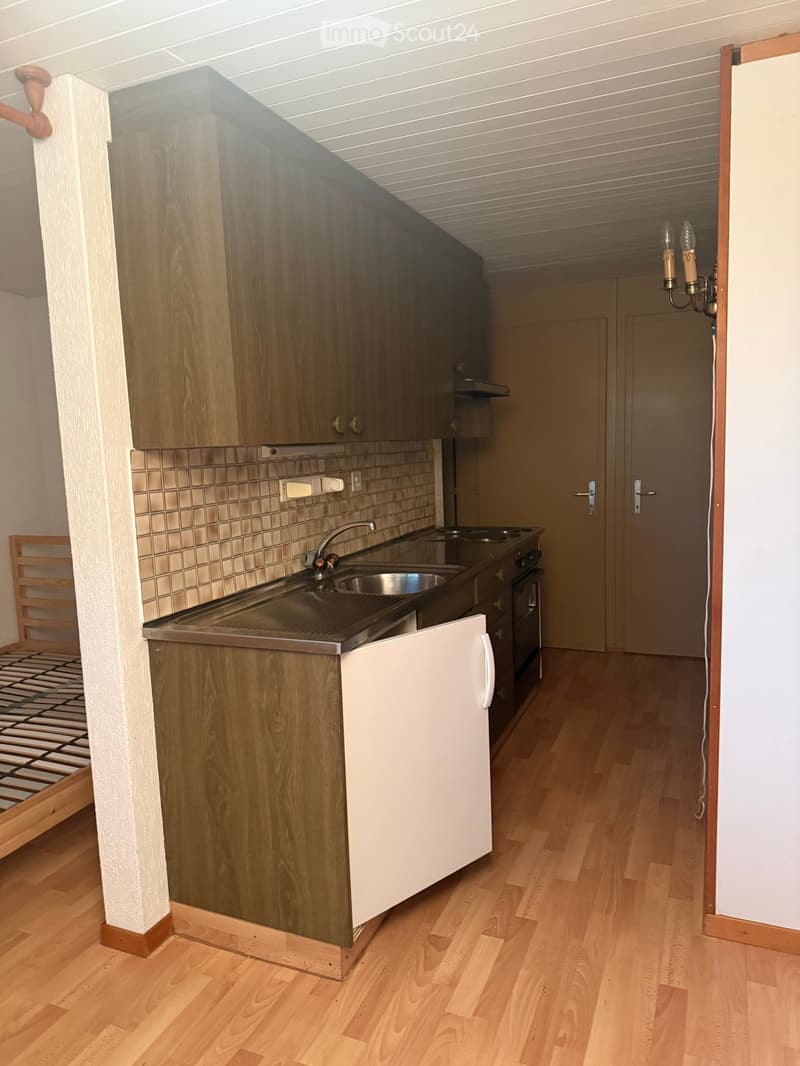 Compact kitchen with wooden cabinets, stainless steel sink, and stove. Wooden flooring and white walls.
