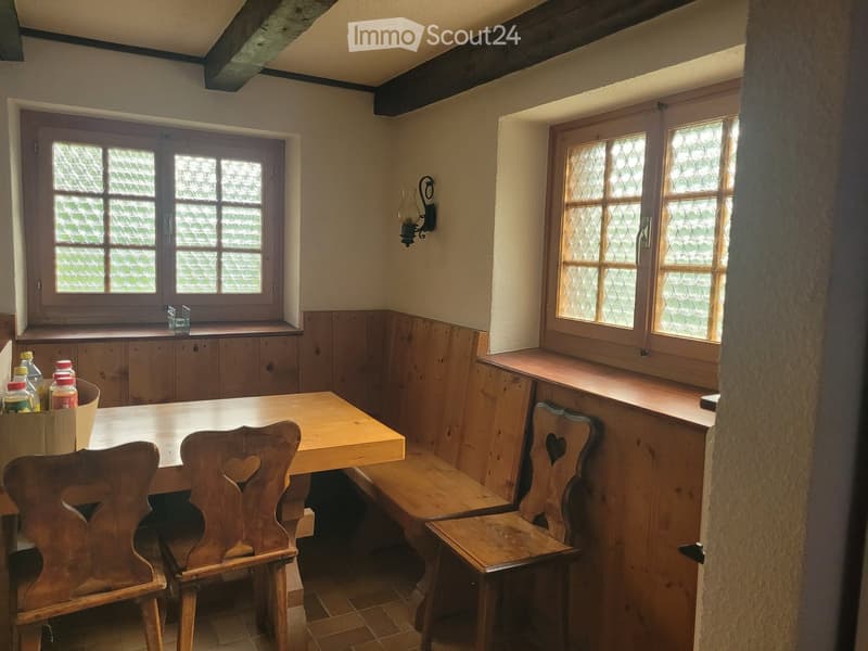 Traditional kitchen with wooden table, chairs, built-in wooden benches, and cabinets. Features stained-glass windows and a wall-mounted lantern-style light fixture.