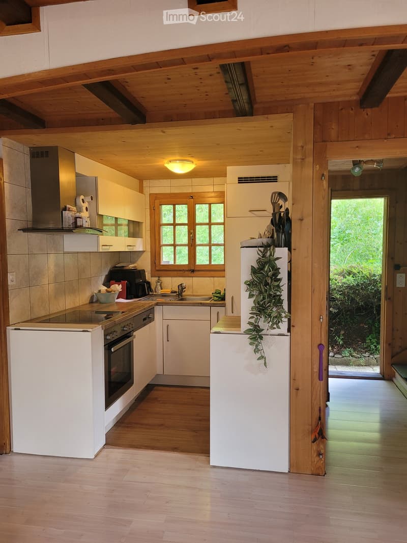 Bright kitchen with wooden beams, white cabinets, stainless steel appliances, and a large window overlooking a green area.
