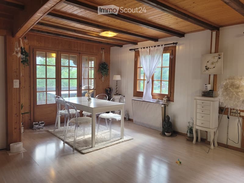 Bright, wooden-floored room with a white dining table and chairs, a lamp, a cabinet, and a decorative rug.