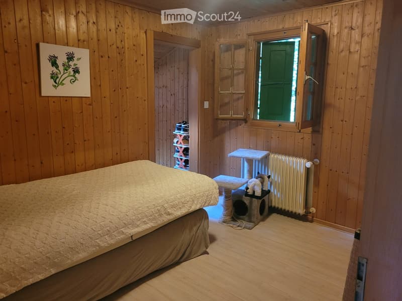 Cozy wooden bedroom with a large bed, a cat tree, a radiator, a small stool, a shoe rack, and a painting on the wall.