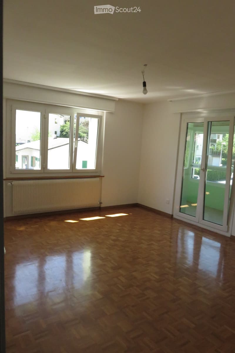 Empty room with wooden flooring, large windows, and a sliding glass door leading to a balcony.