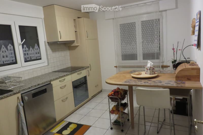Bright kitchen with light-colored cabinets, granite countertop, built-in oven and dishwasher, and a small round table with chairs.