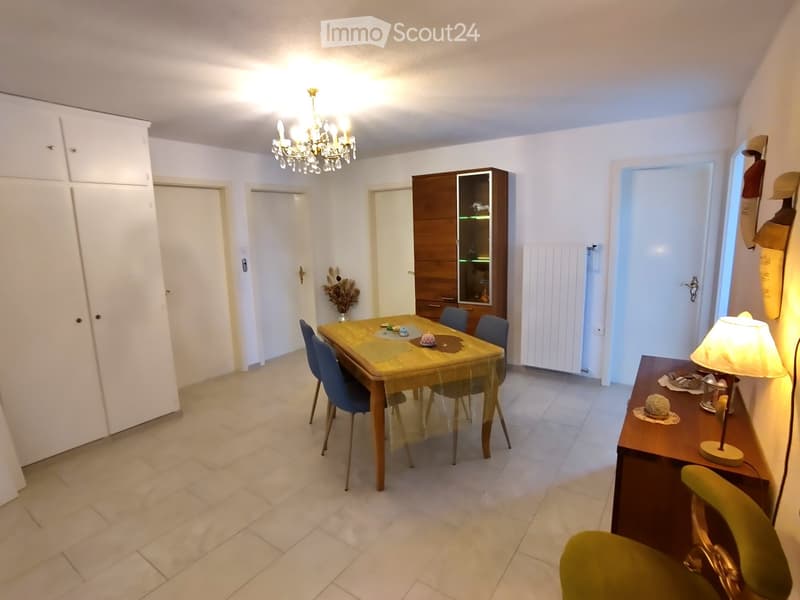 Dining room with a wooden dining table, blue chairs, a wooden cabinet, a chandelier, and a side table with a lamp.