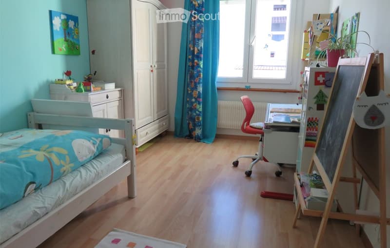 Brightly colored children's bedroom with a single bed, wardrobe, desk, chair, and various decorations including a picture frame and a blackboard.