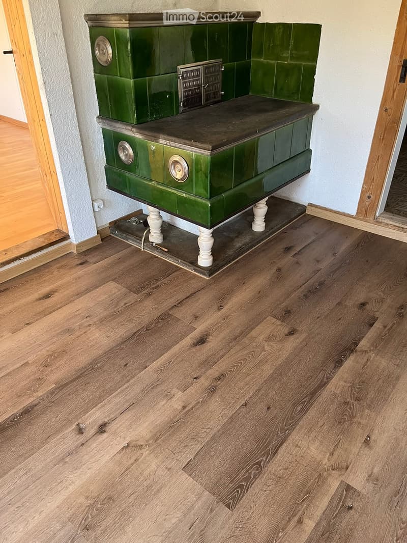 A hallway with wooden flooring and a green tiled fireplace with white legs and a black top.