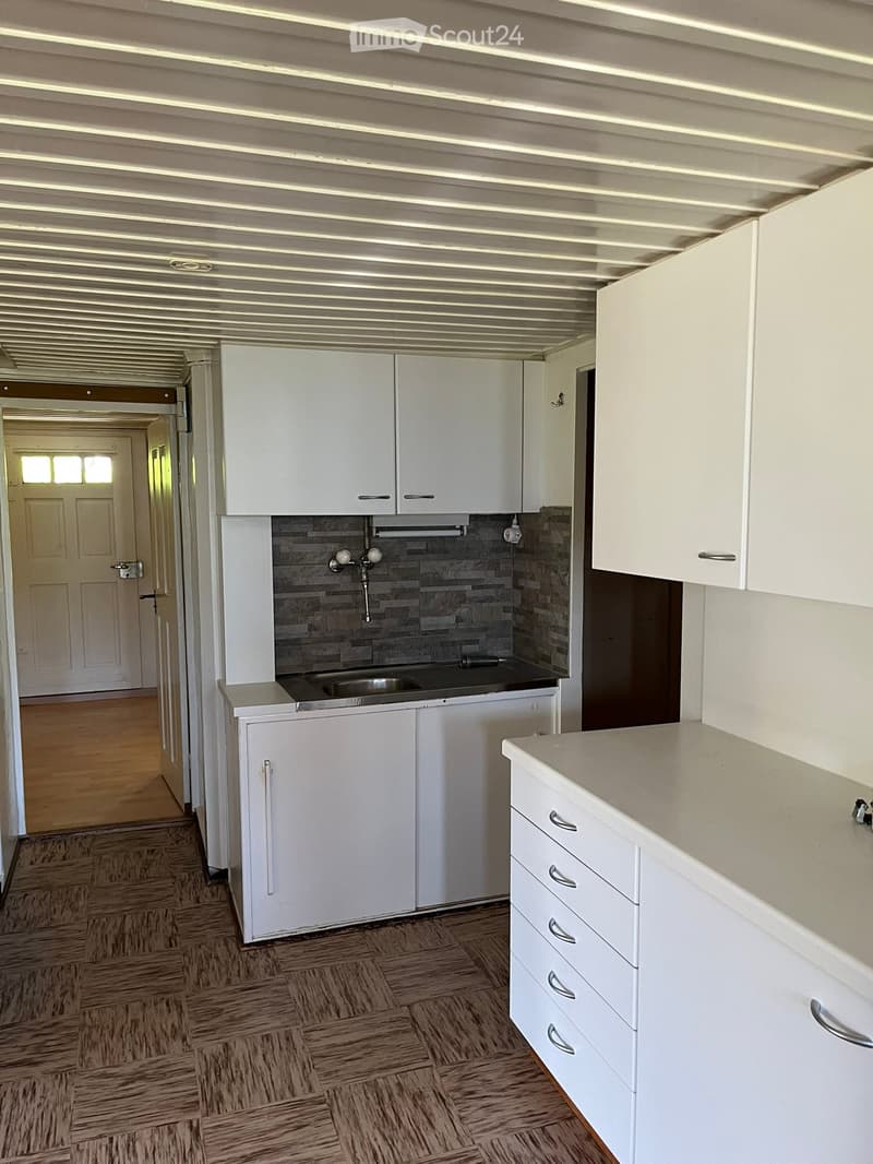 Modern kitchen with white cabinets, a sink, and a tiled backsplash. The floor is wooden, and the ceiling has a ribbed design.