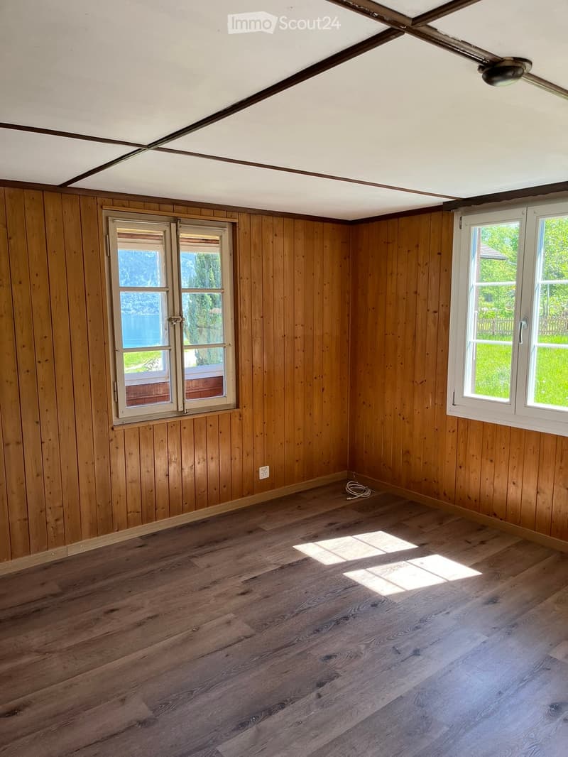 Empty room with wooden walls and floor, two windows, and a ceiling fan. No furniture or equipment present.