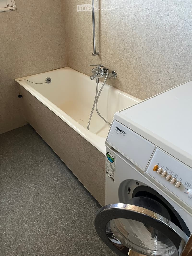 Bathroom with a bathtub, faucet, and a washing machine placed next to it.