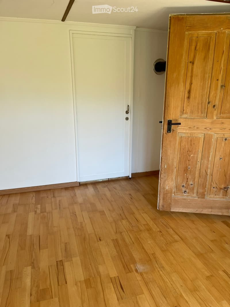 Empty room with wooden flooring and white walls, featuring a closed wooden door and a white door frame.