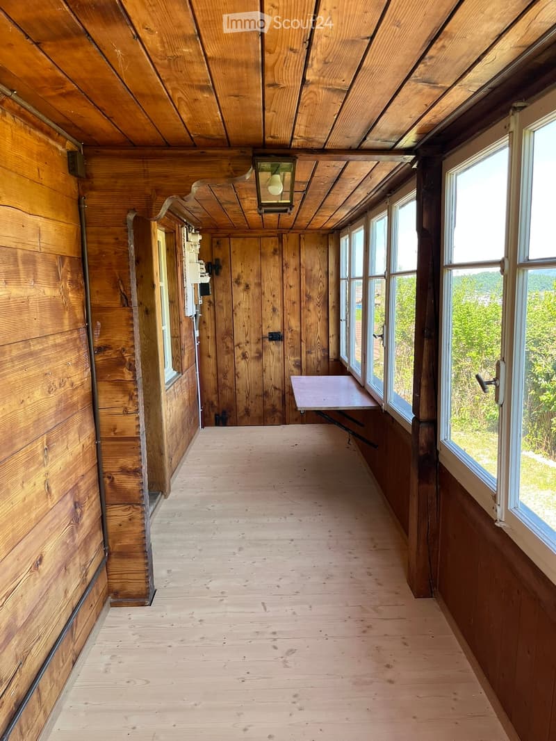 Wooden hallway with exposed beams, large windows, and a small table near the end.