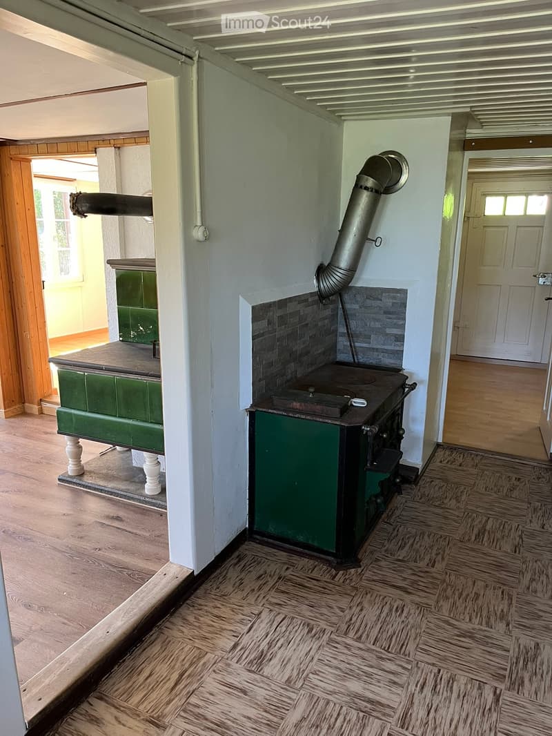 A kitchen with a vintage stove and a wooden table, featuring wooden flooring and white walls.