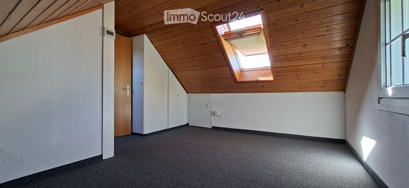 Empty room with wooden slanted ceiling, grey carpet, white walls, and a skylight window.