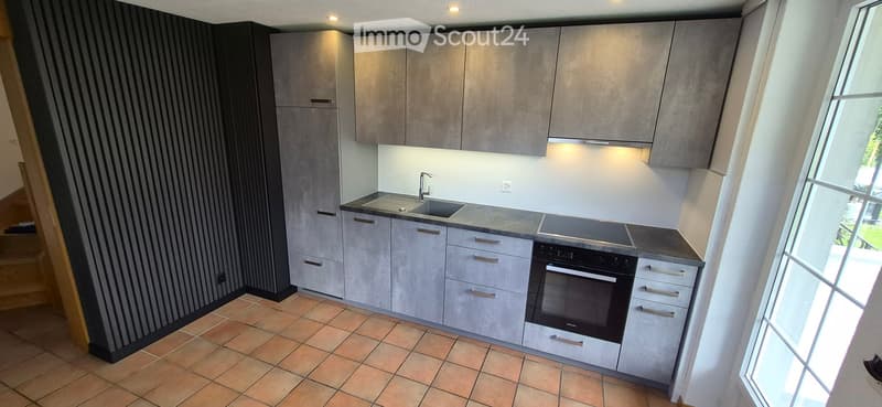 Modern kitchen with grey cabinets, a sink, a faucet, and an oven, featuring tiled flooring and large windows.