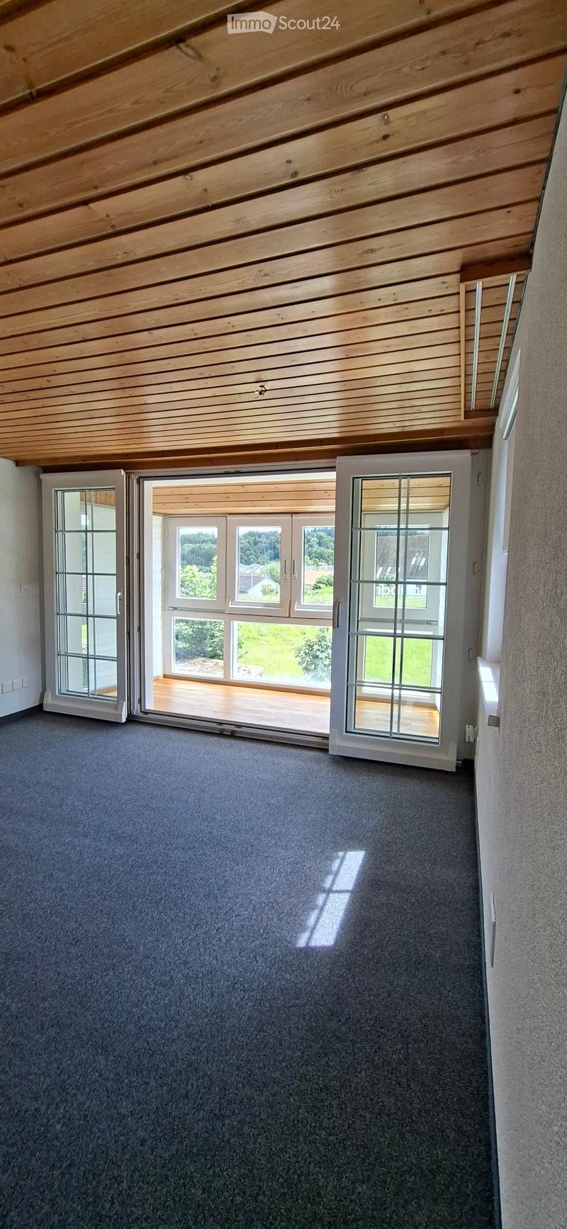 Empty room with grey carpet, wooden slanted ceiling, and large sliding glass doors leading to a wooden deck.