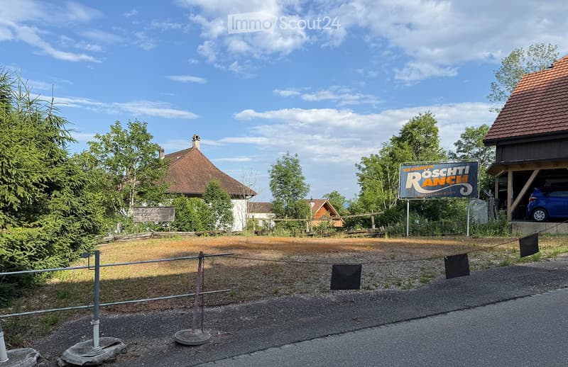 A rural ranch with a fenced entrance, a sign reading "Röschti Ranch," and a garage with a parked car.