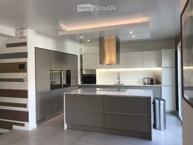 Modern kitchen with sleek grey and white cabinets, stainless steel appliances, a central island, and built-in lighting.