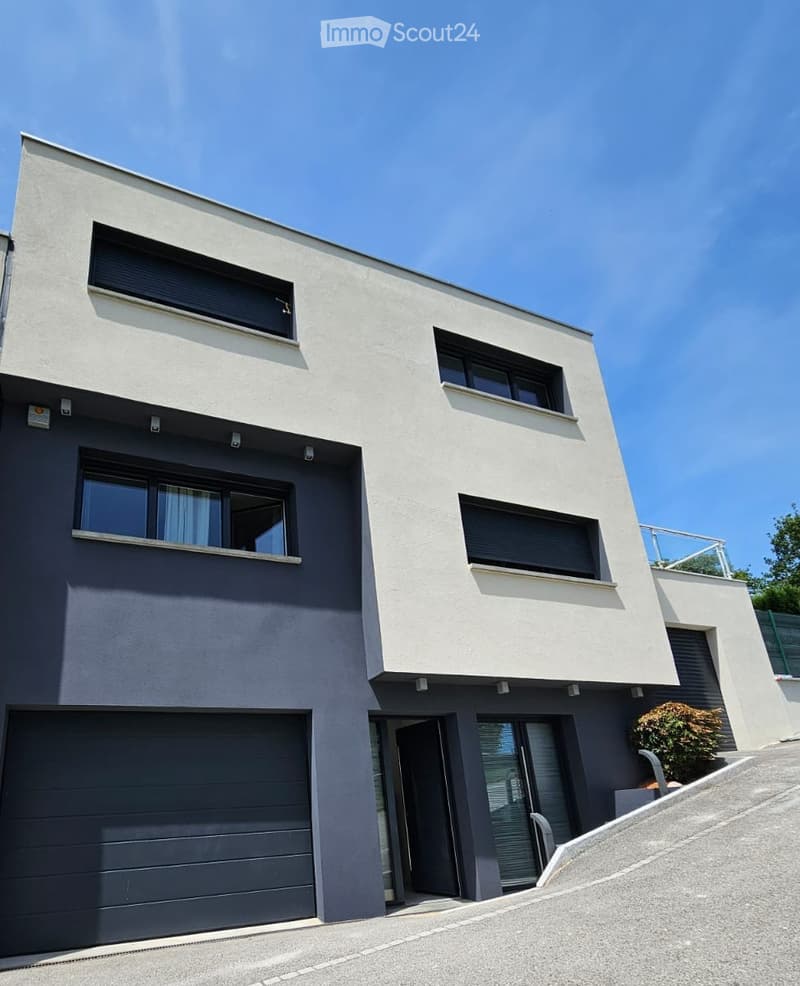 Modern two-story house with a combination of white and dark grey exterior walls, large windows, and a garage.