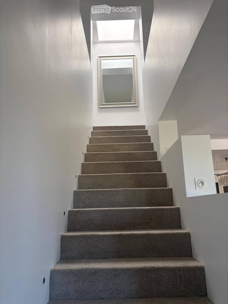 Modern staircase with carpeted steps, white walls, and a large mirror on the wall.