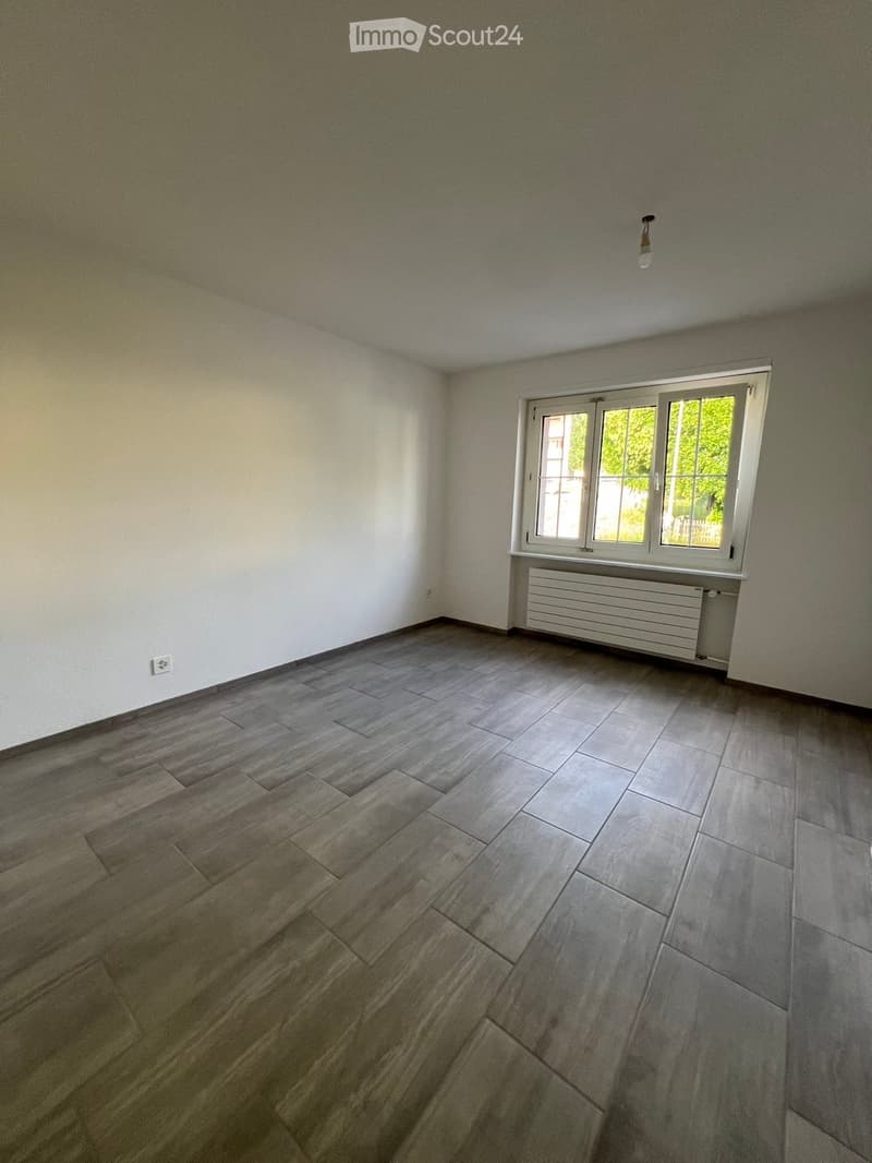 Empty room with wooden and tiled flooring, white walls, a window with white frame, radiator, and a light fixture on the ceiling.