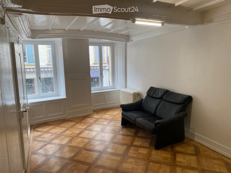 empty room, wooden floor, white walls, windows with blue shutters, black leather couch, white door
