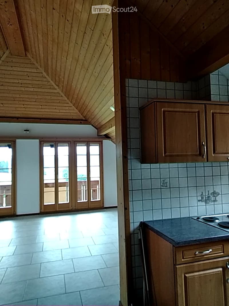 Top-down view of a kitchen area with wooden cabinets, tiled floor, and a window. Below, a wooden staircase leads up, with a glass door visible at the top.