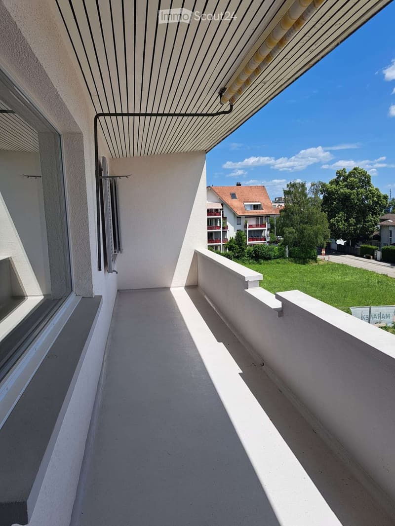 Balcony with white railings, striped awning, and view of a green lawn and neighboring buildings.