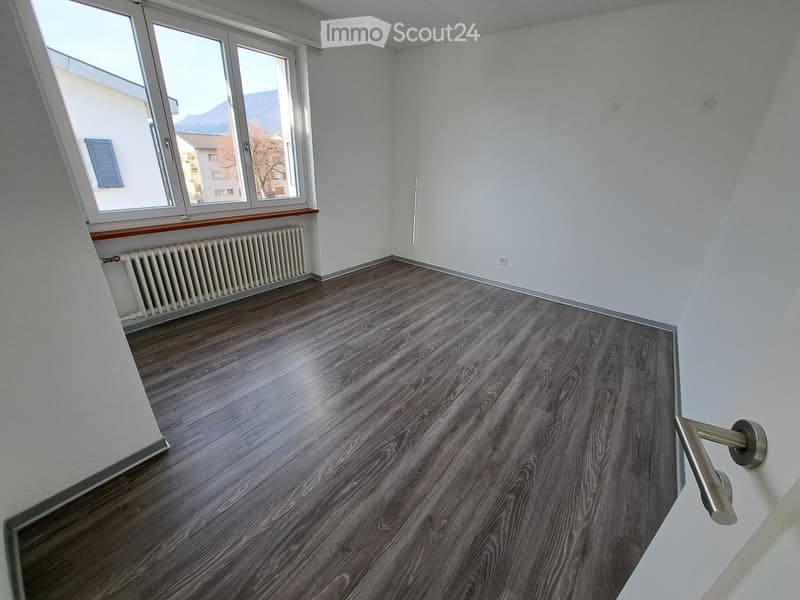 Empty room with wooden flooring, white walls, large windows, radiator, and a metal handrail.