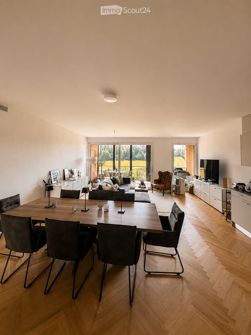 Modern living and dining area with wooden flooring, large windows, a sofa, coffee table, dining table with chairs, and a TV stand.