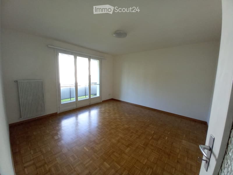 Empty room with wooden flooring, white walls, large sliding glass door leading to a balcony, and a radiator on one wall.