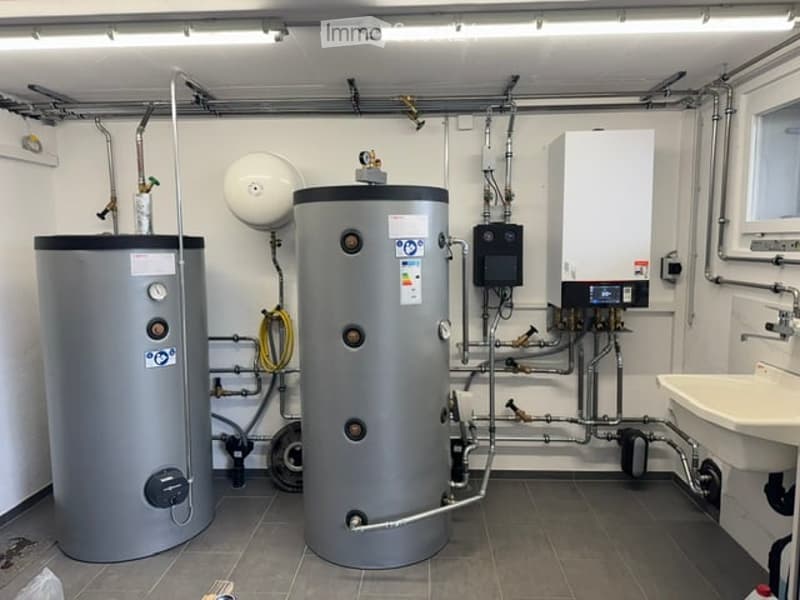 Modern bathroom utility area with two water heaters, a sink, and various pipes and valves.