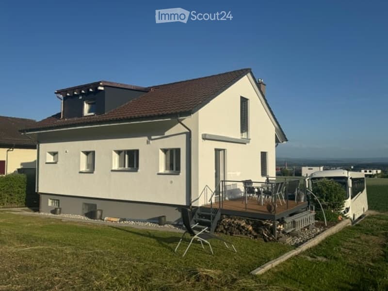 Single-story house with a modern design, white exterior, brown roof, and a small patio with outdoor furniture.
