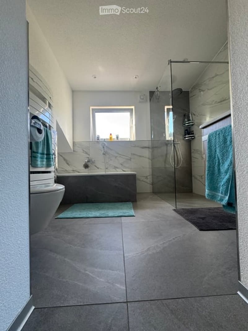 Modern bathroom with a large window, marble accents, a bathtub, toilet, shower, and towels.