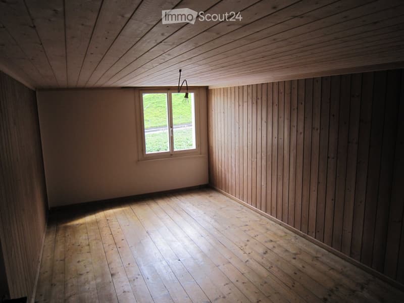 Empty room with wooden walls, wooden floor, and a single window letting in natural light. No furniture or equipment present.