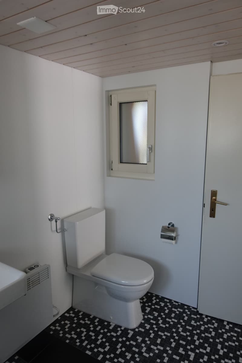 Modern bathroom with white walls, black and white checkered floor, toilet, toilet paper holder, and radiator.