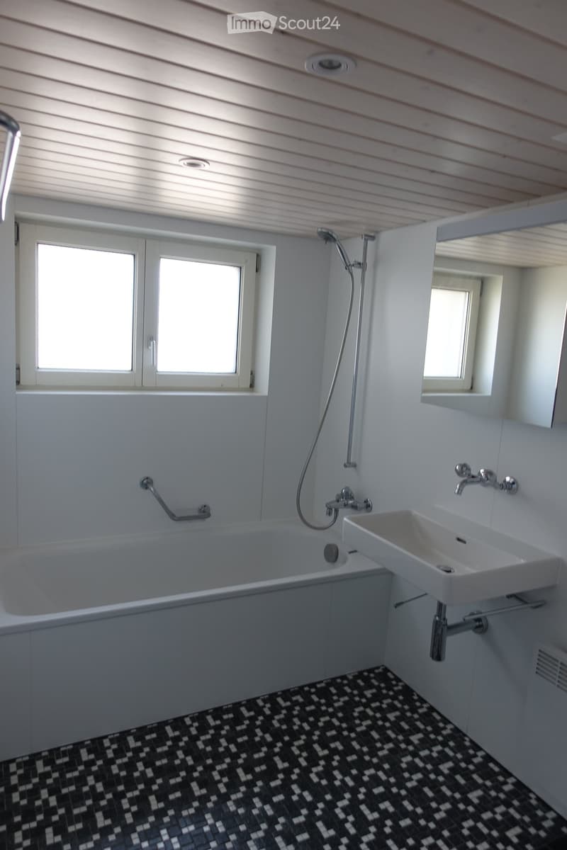 Modern bathroom with white walls, black and white tiled floor, bathtub, sink, and showerhead.