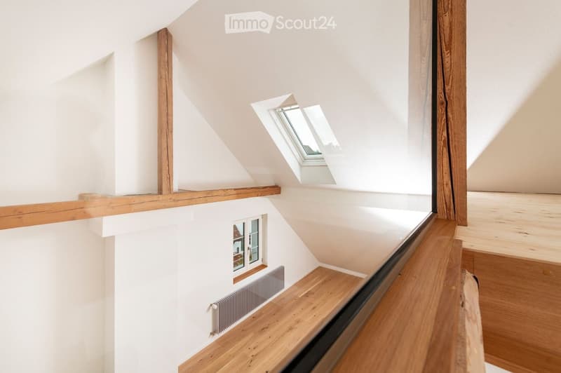 Empty attic space with wooden flooring, white walls, exposed wooden beams, and skylight windows allowing natural light.