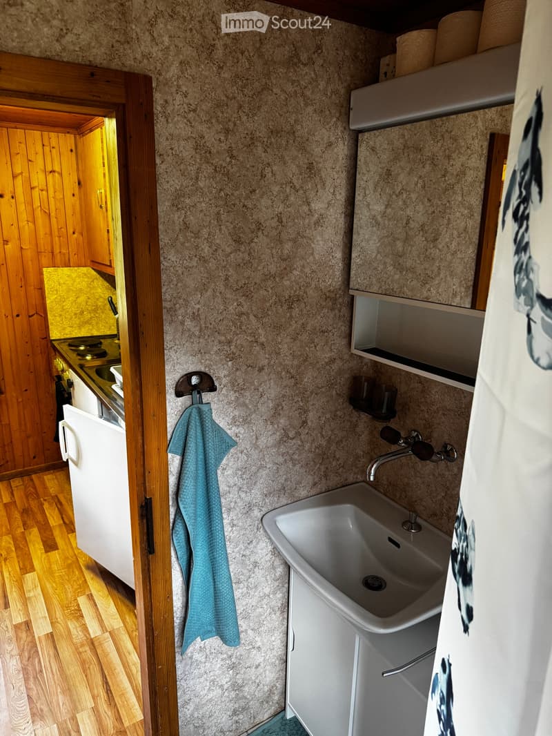 Bathroom with a white sink, faucet, cabinet, and a blue towel hanging on a hook. Wooden floor and textured walls.