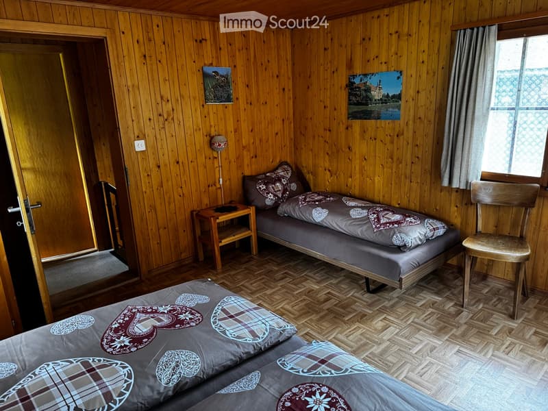 Cozy wooden bedroom with two single beds, nightstand, chair, and artwork on the walls.