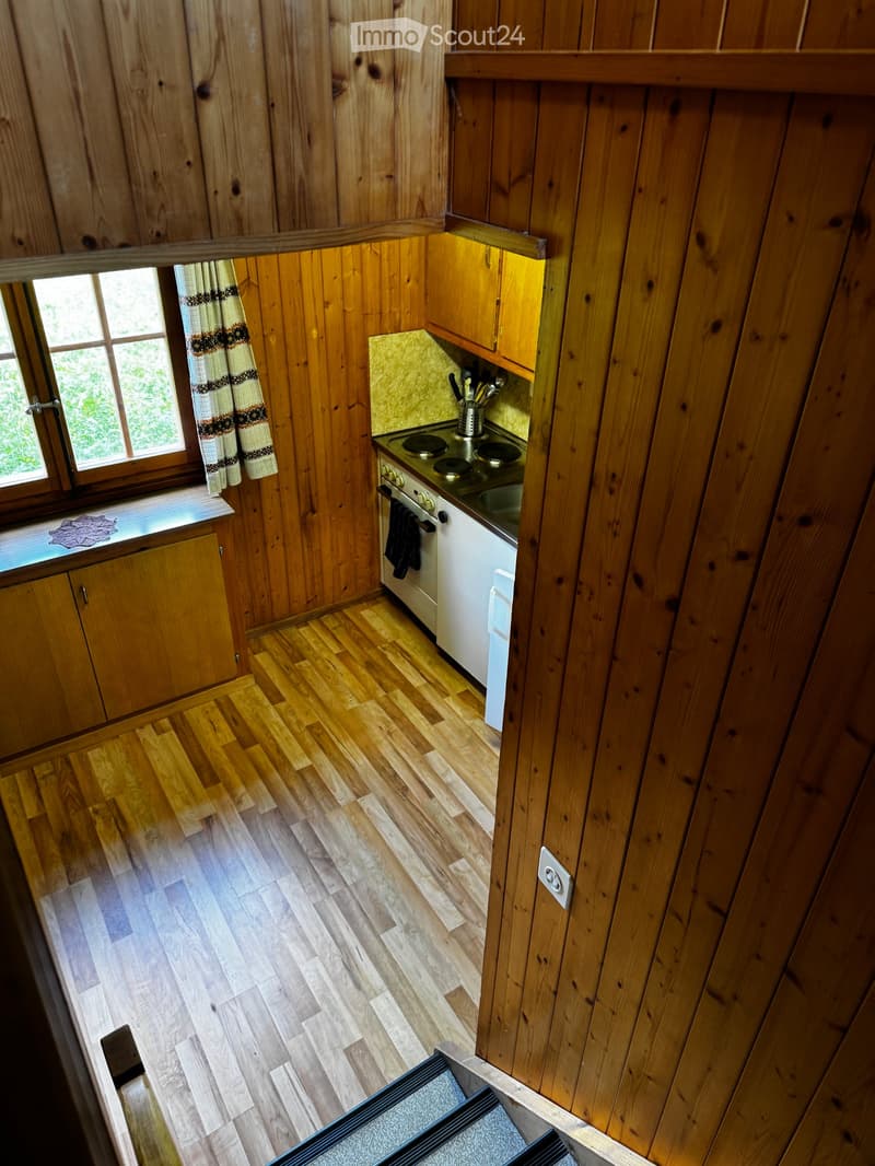 Cozy kitchen with wooden walls and flooring, featuring a stove, oven, cabinets, and a window with a curtain.
